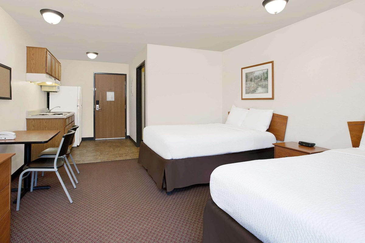 Ett hotellrum med en säng, ett skrivbord med en stol, ett litet pentry och en dörr.