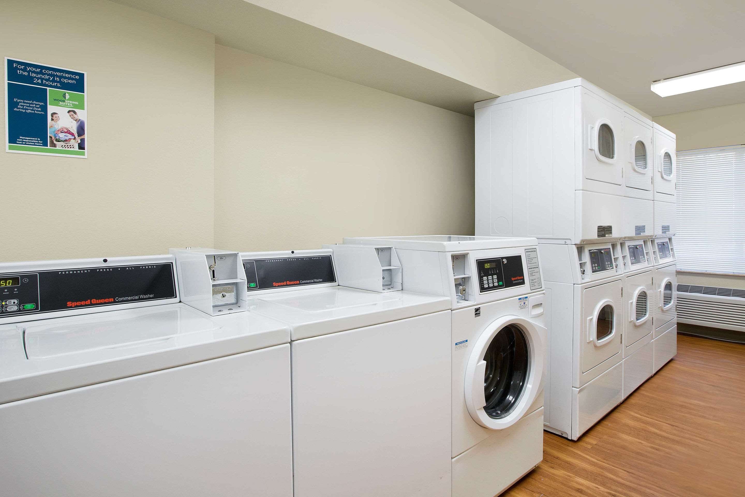 A laundry facility with multiple washing machines and dryers, a control panel, and a poster on the wall.