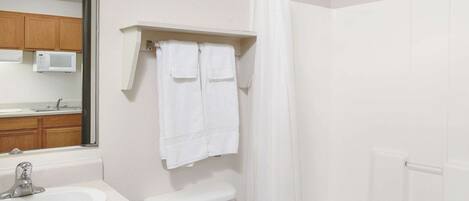 Un baño con lavamanos, inodoro y cortina de ducha blancos. Hay un espejo sobre el lavamanos y un perchero sobre el inodoro.