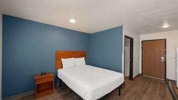 Une chambre à coucher avec une tête de lit en bois, un couvre-lit blanc, une table de chevet et une porte sur le côté droit.
