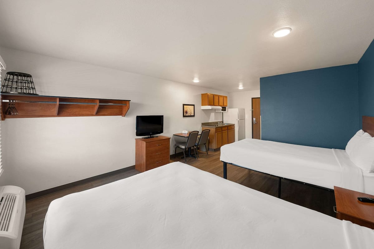Ein Hotelzimmer mit zwei Betten, einem Schreibtisch mit Stuhl, einer Küchenzeile und einem Fernseher.