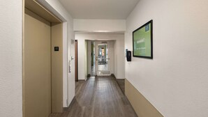Un couloir d’hôtel avec un plancher en bois, un panneau encadré accroché au mur et une porte ornée d’un symbole en forme d’étoile.