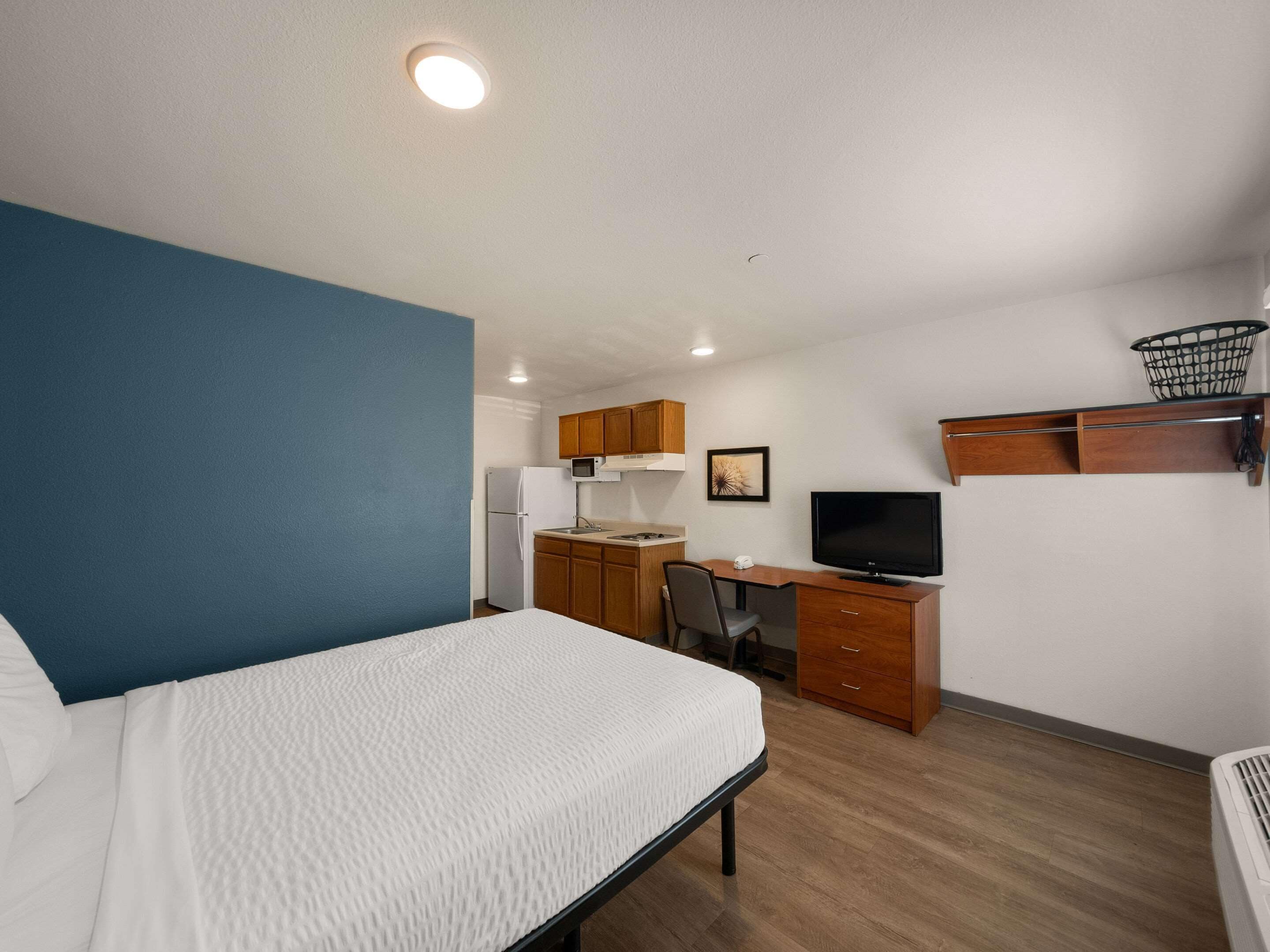 Habitación de hotel con cama, escritorio, silla, televisor, microondas y una pequeña cocina.