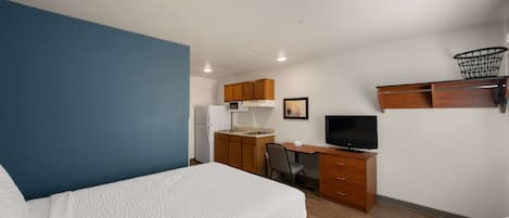 Habitación de hotel con cama, escritorio, silla, televisor, microondas y una pequeña cocina.