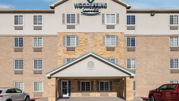 Un hôtel à la façade en pierre, doté d’une entrée centrale et d’une enseigne indiquant « Woodspring Suites ».