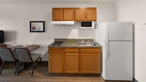 Une cuisine compacte dotée de meubles en bois, d’un four à micro-ondes, d’un réfrigérateur, d’un plan de travail en granit, d’un évier et d’un coin repas avec des chaises.