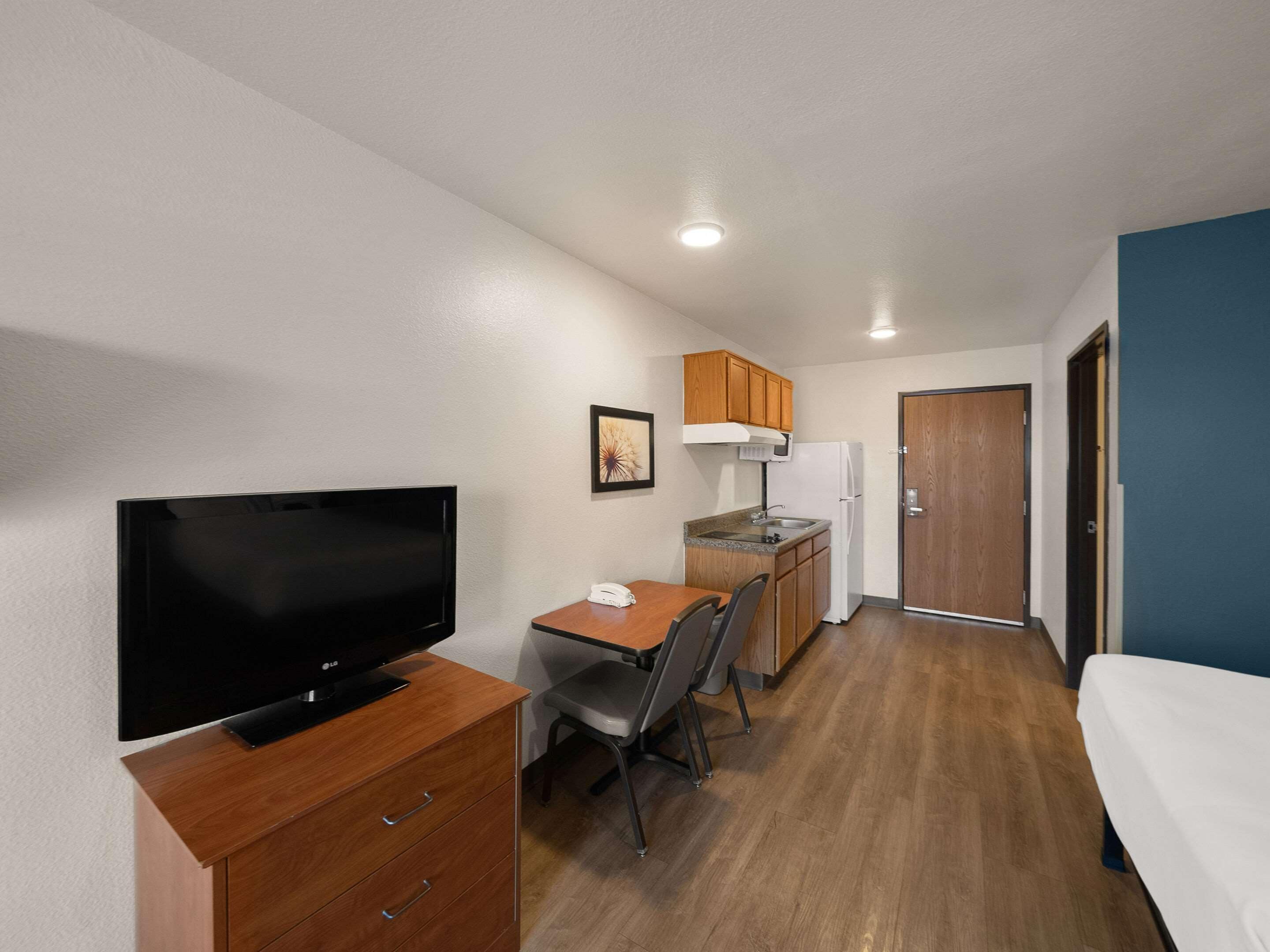 Une chambre d’hôtel de taille réduite, équipée d’une télévision, d’une petite kitchenette, d’un coin repas et d’un lit.