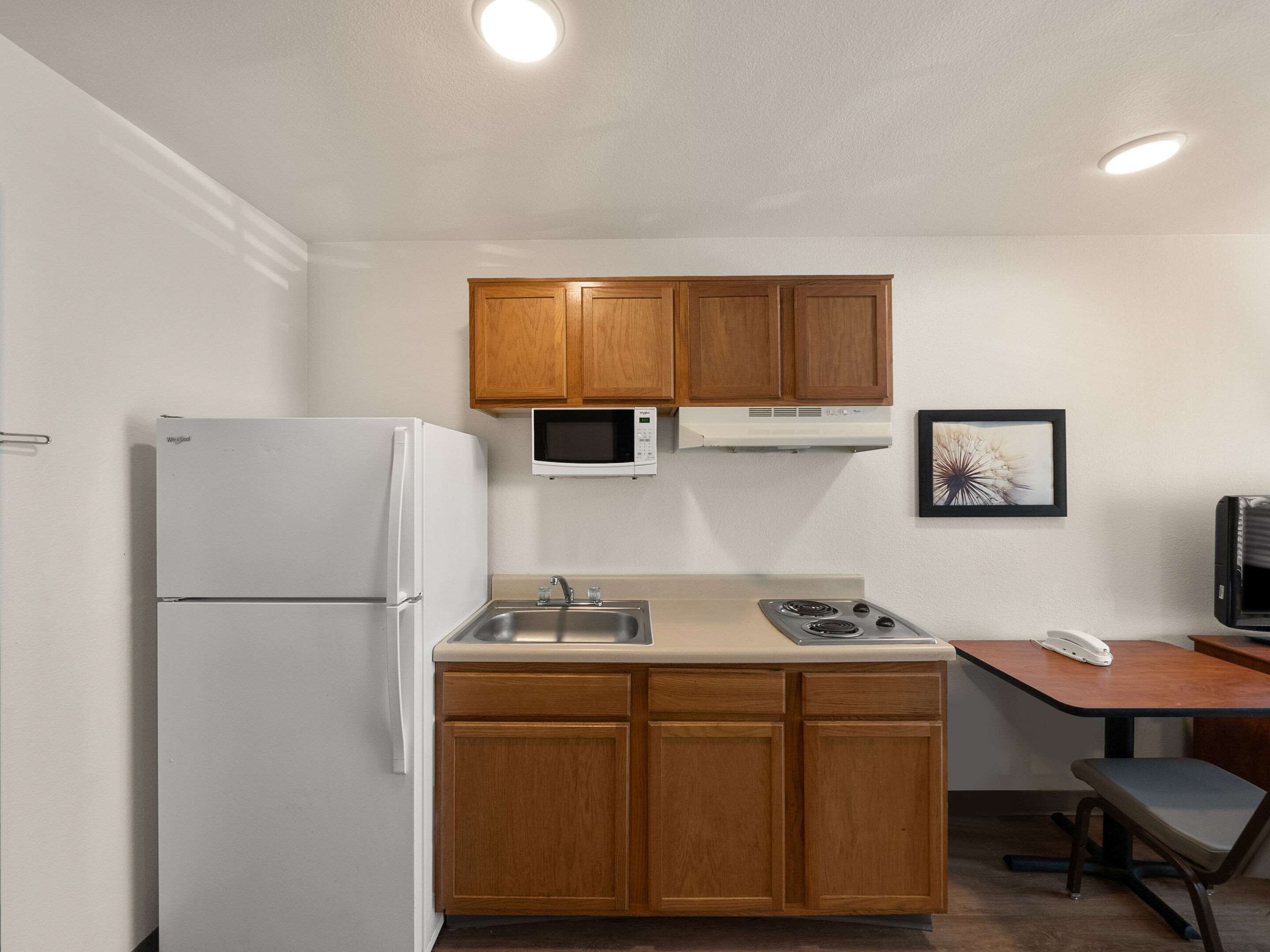 Une cuisine compacte avec des meubles de rangement en bois, un réfrigérateur, un four à micro-ondes, une cuisinière et une petite table à manger avec une chaise.