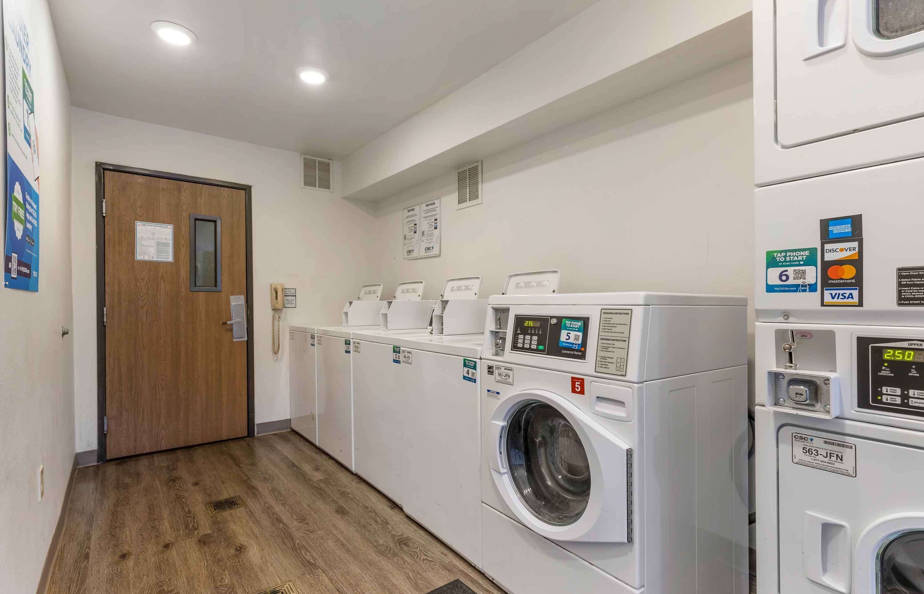 A laundry facility with multiple washing machines, a wooden door, and a wall-mounted information board.