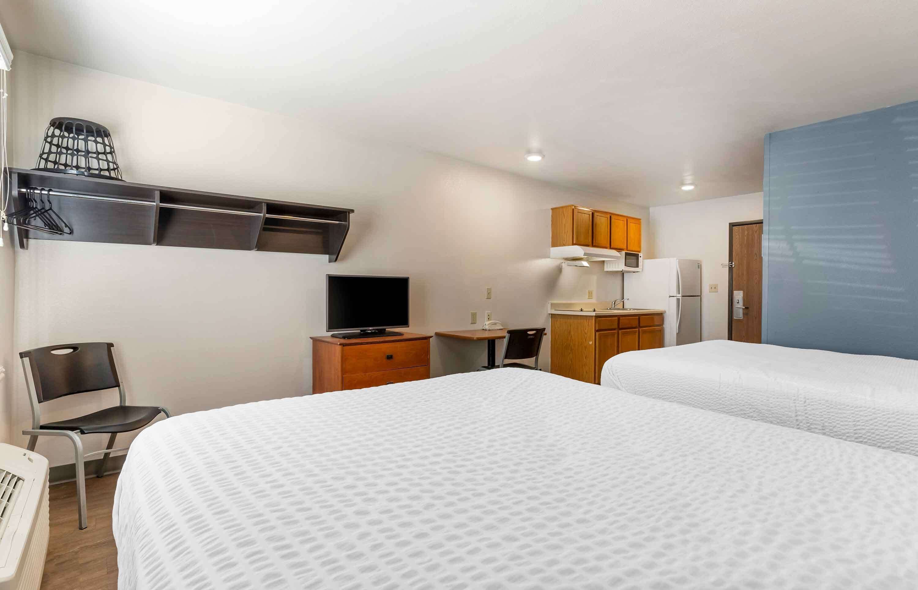 Een hotelkamer met twee bedden, een bureau, een stoel, een televisie en een kledingkast.