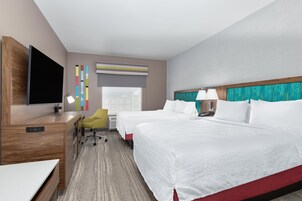 Habitación de hotel con cama, escritorio, silla, televisor y ventana con persianas.