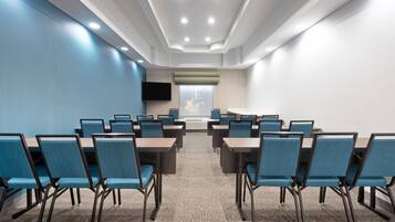 Une salle de conférence avec des rangées de tables et de chaises, un téléviseur à écran plat et une grande fenêtre donnant sur un paysage.