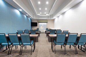 Une salle de conférence avec des rangées de tables et de chaises, un téléviseur à écran plat et une grande fenêtre donnant sur un paysage.