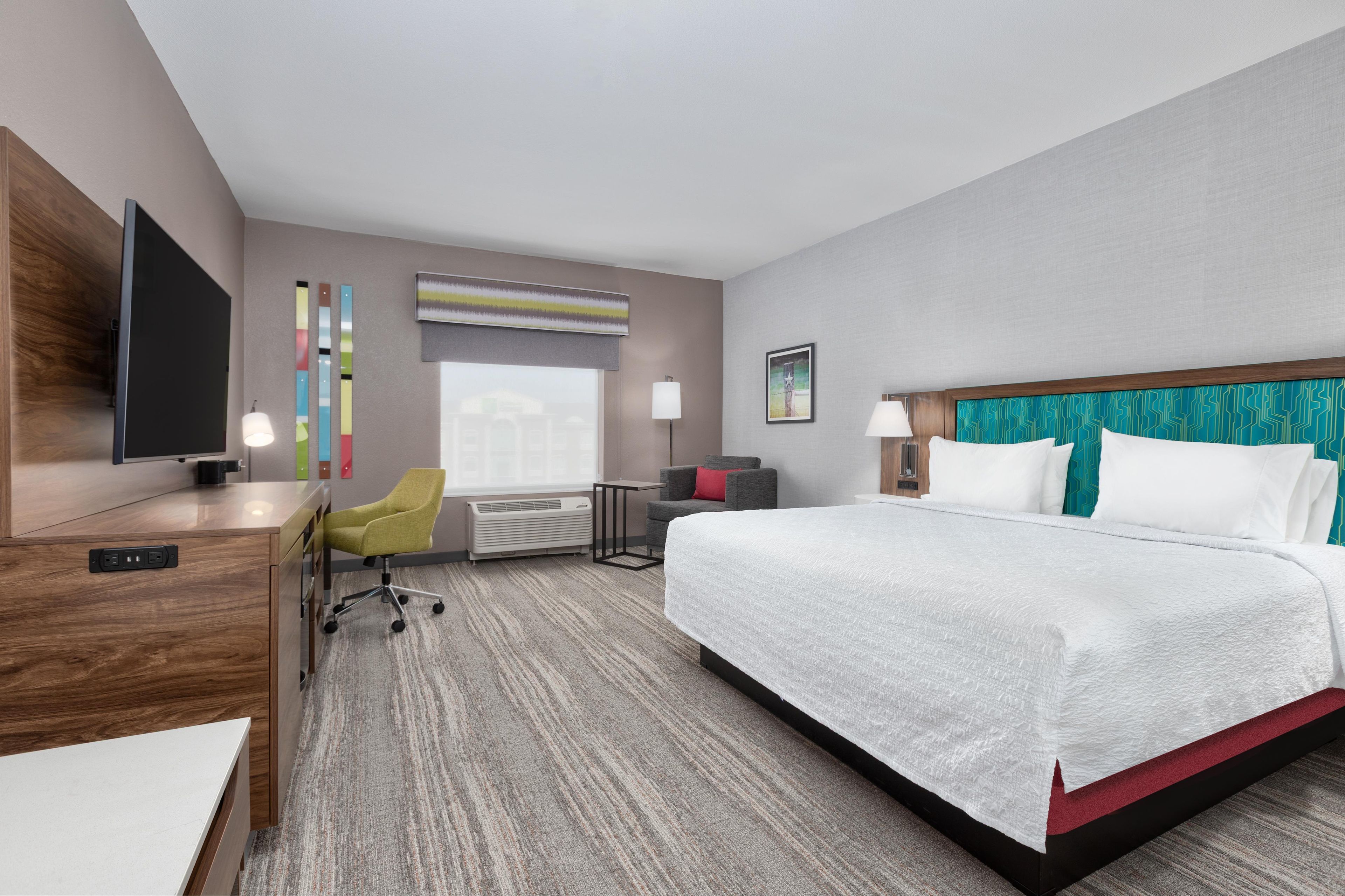 A hotel room with a large bed, a desk, a chair, a television, and a window.