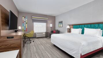 A hotel room with a large bed, a desk, a chair, a television, and a window.