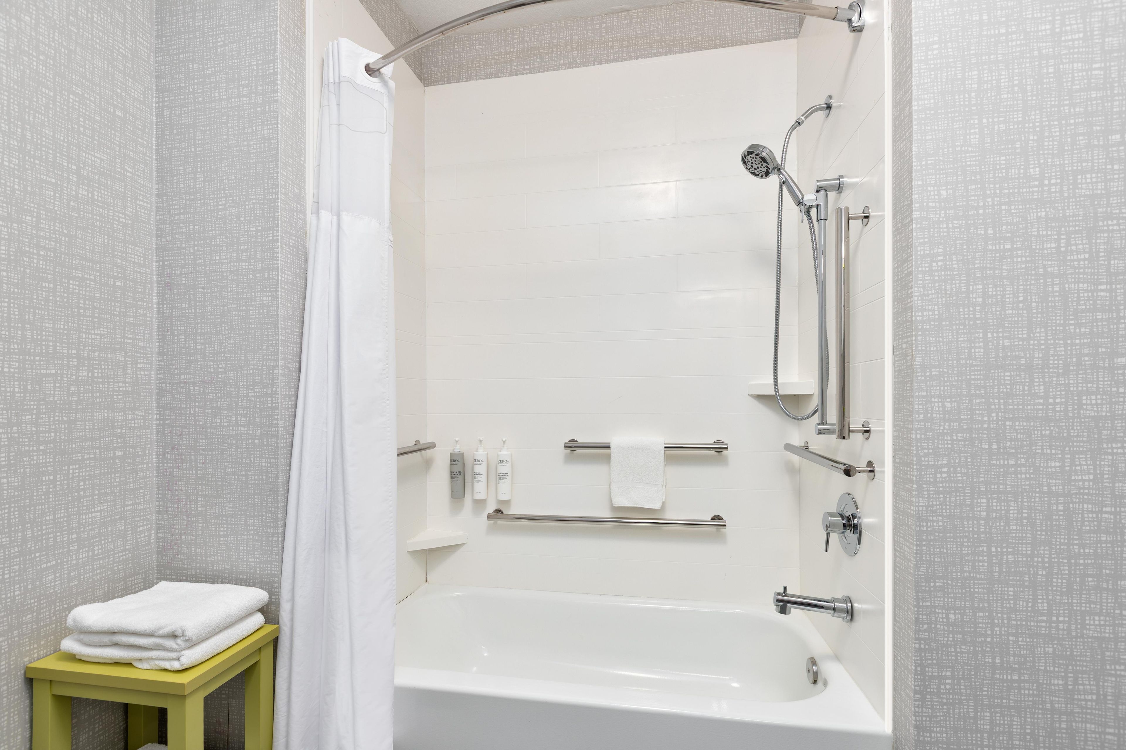 A modern bathroom with a bathtub, shower, and handrails.