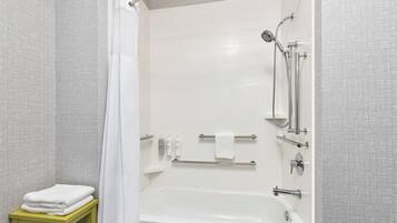 A modern bathroom with a bathtub, shower, and handrails.
