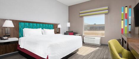 A hotel room with a large bed, two bedside tables, a desk, a chair, a window with a view, and a flat-screen TV.