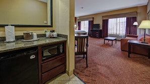 A hotel room with a kitchenette, a dining area, a living room with a sofa and a TV, and a large window with curtains. - Hampton Inn Corsicana (Corsicana)