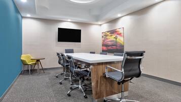 Un salón de conferencias con una mesa larga, seis sillas, un televisor y un cuadro de colores en la pared.