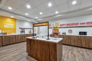 Un área de desayuno con un cartel que dice 'Happy Breakfast Starts Here' y una presentación de frutas y pasteles.