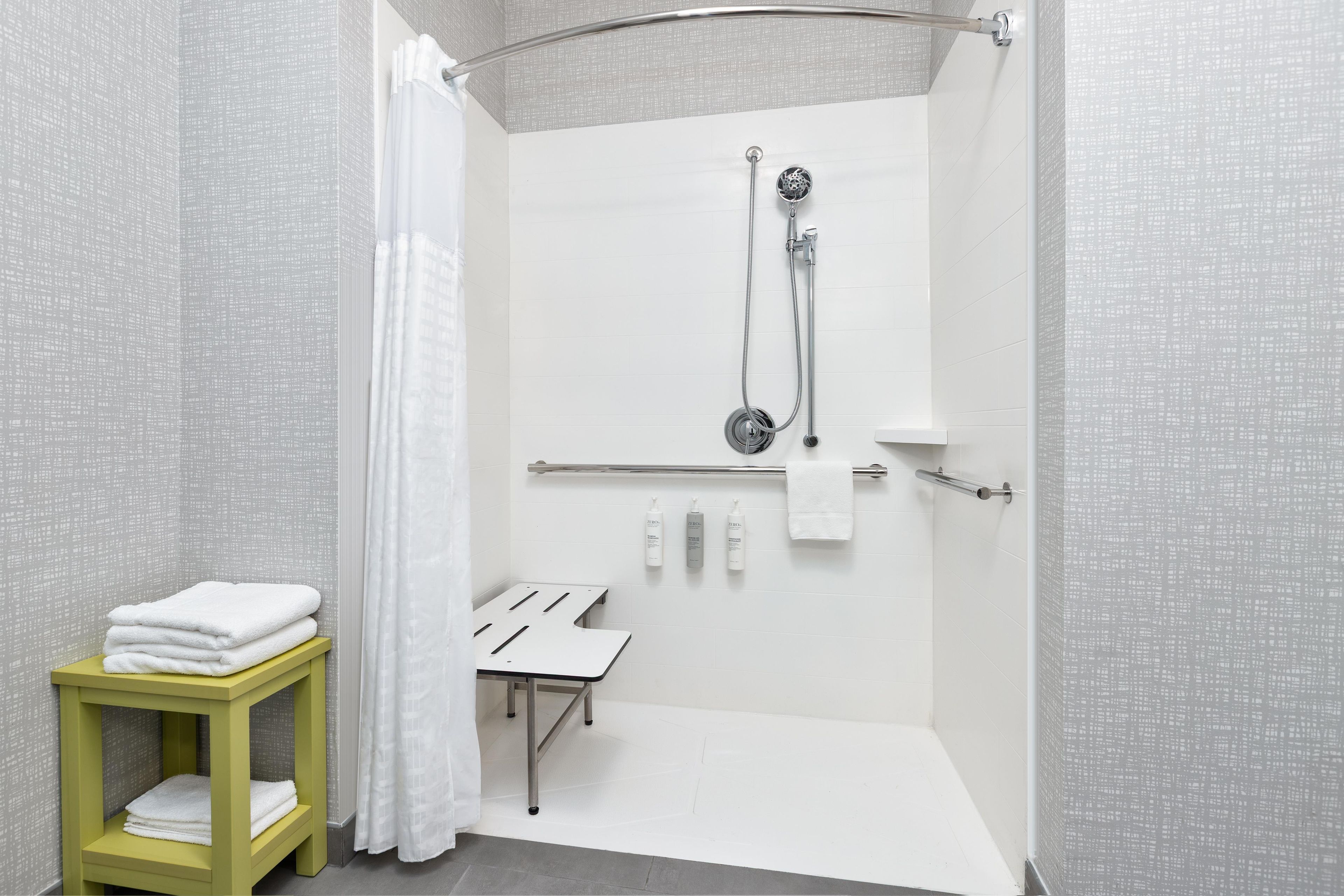 A modern bathroom with a shower, a towel rack, and a small table with towels.