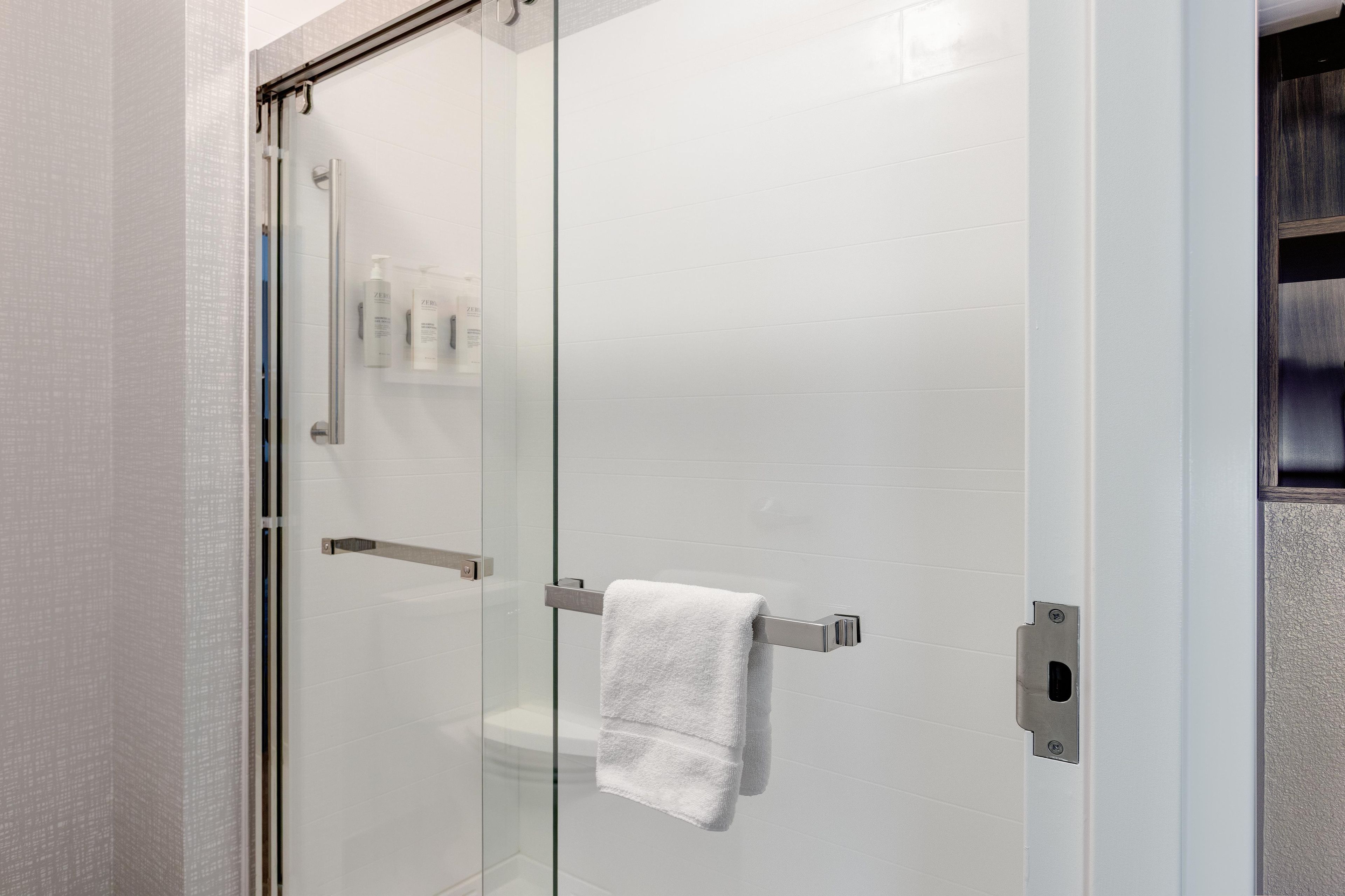 A glass-enclosed shower stall with a white towel hanging on a metal towel bar.