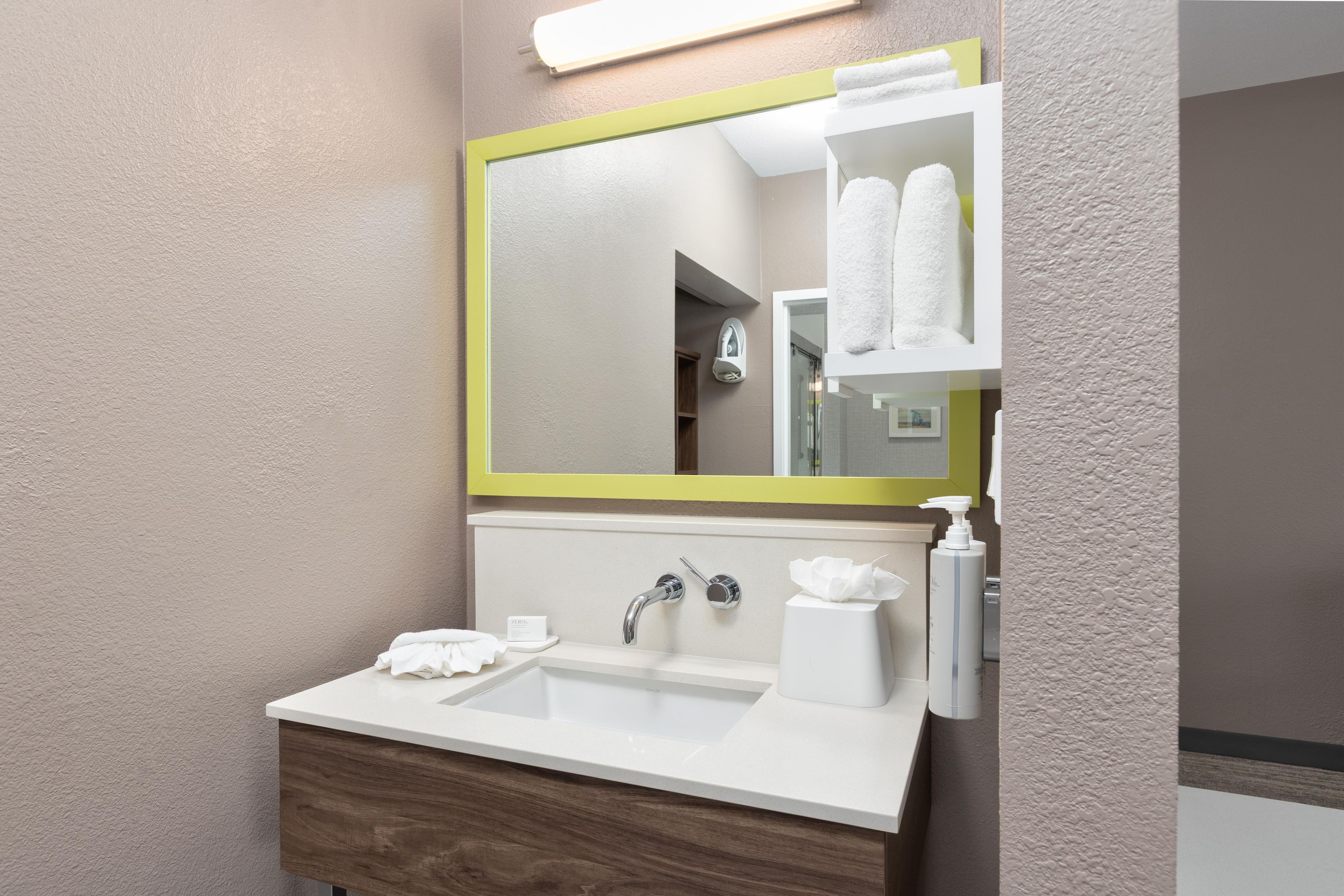A modern bathroom with a white sink, a mirror with a yellow frame, and a towel dispenser.