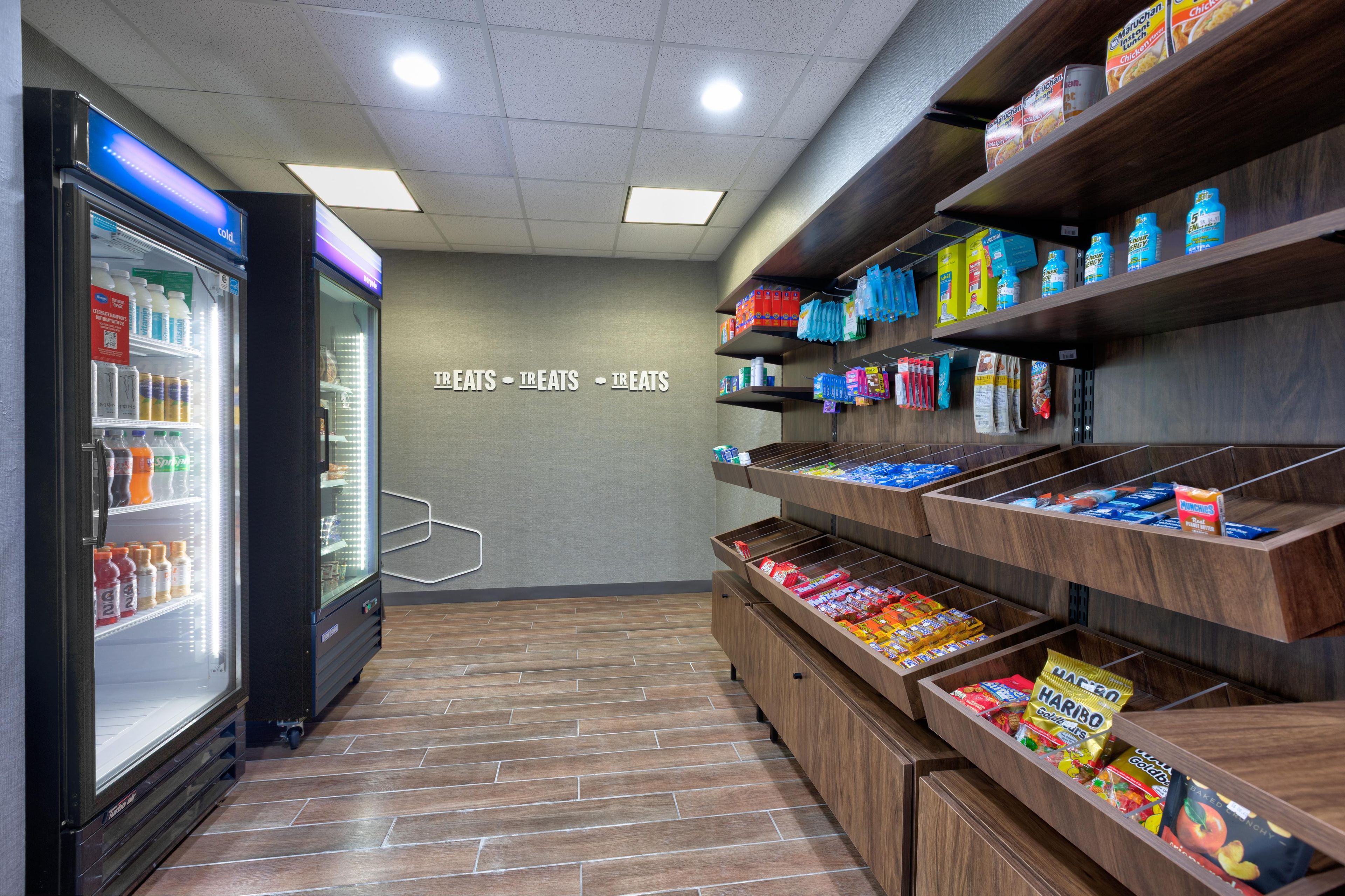 A self-service snack area with refrigerated drinks and a variety of packaged snacks on shelves.