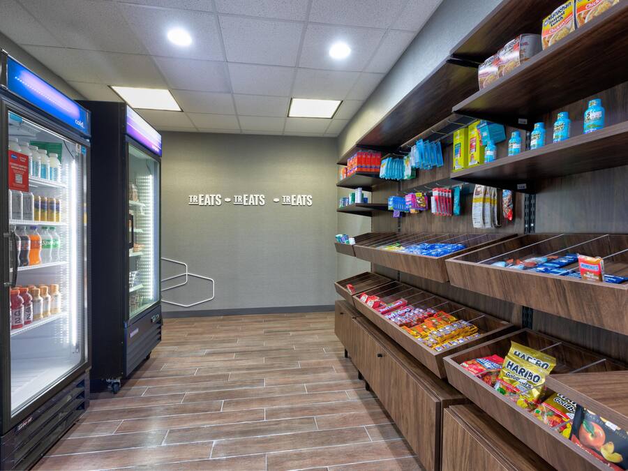 A self-service snack area with refrigerated drinks and a variety of packaged snacks on shelves.