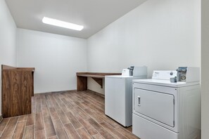 A laundry room with two front-loading washers, a wooden bench, and a ceiling light. - Hampton Inn Corsicana (Corsicana)