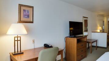 Habitación de hotel con un escritorio de madera, una silla, un televisor sobre un mueble de madera, un teléfono, un cuadro en la pared y un espejo.
