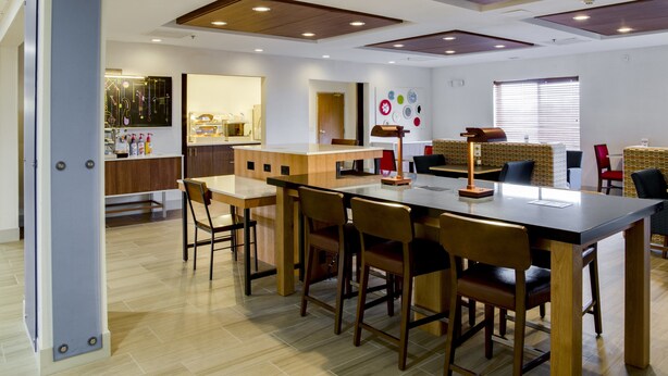A modern dining area with a long table and chairs, a kitchen in the background, and a wall with colorful circular decorations. - Holiday Inn Express Hotel & Suites Jacksonville by IHG (Jacksonville)