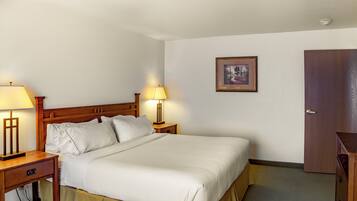 A hotel room with a bed, two bedside tables with lamps, a nightstand, a framed picture on the wall, and a wooden door.