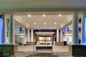 Un espace extérieur abrité, doté de colonnes, d’un banc et de l’entrée d’un bâtiment.