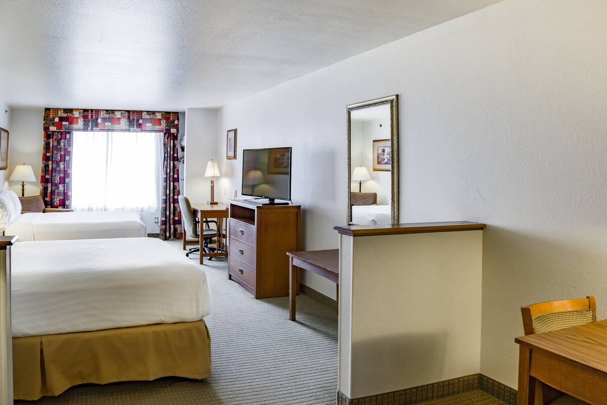 A hotel room with two beds, a desk, a television, and a mirror.