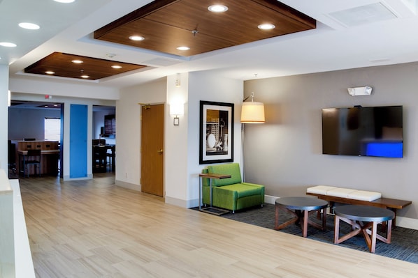 A hotel lobby with a wooden ceiling, a green armchair, a sofa, a TV, and a small table.
