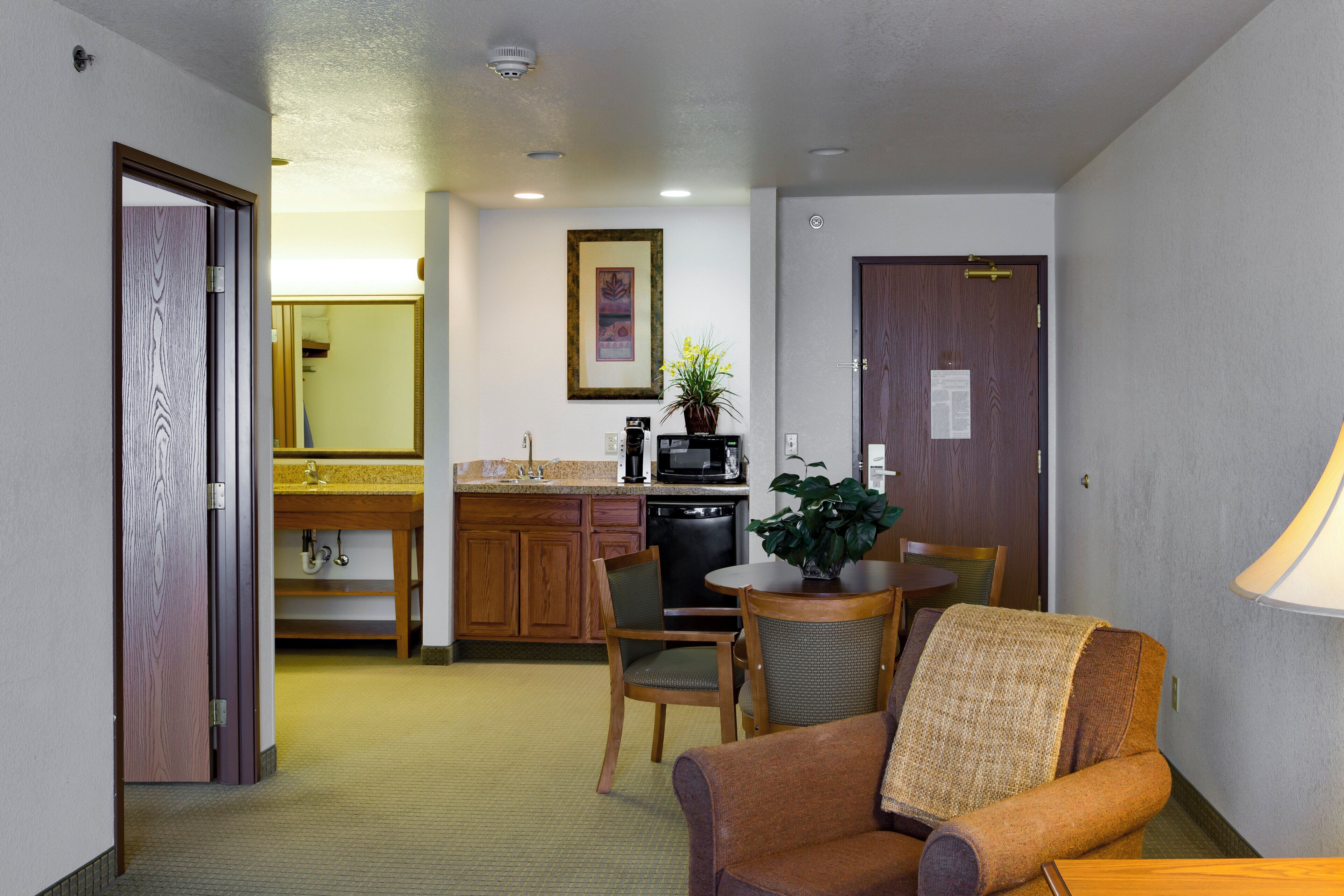Een compacte hotelkamer met kitchenette, een zithoek met tafel en stoelen, en een eenpersoonsbed.