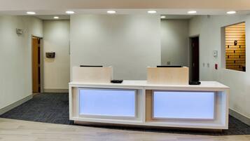 Un mostrador de recepción con dos paneles iluminados, piso alfombrado y una pared de madera con estantería empotrada.