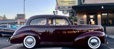 A vintage car parked in front of a motel with a 'Welcome' sign.