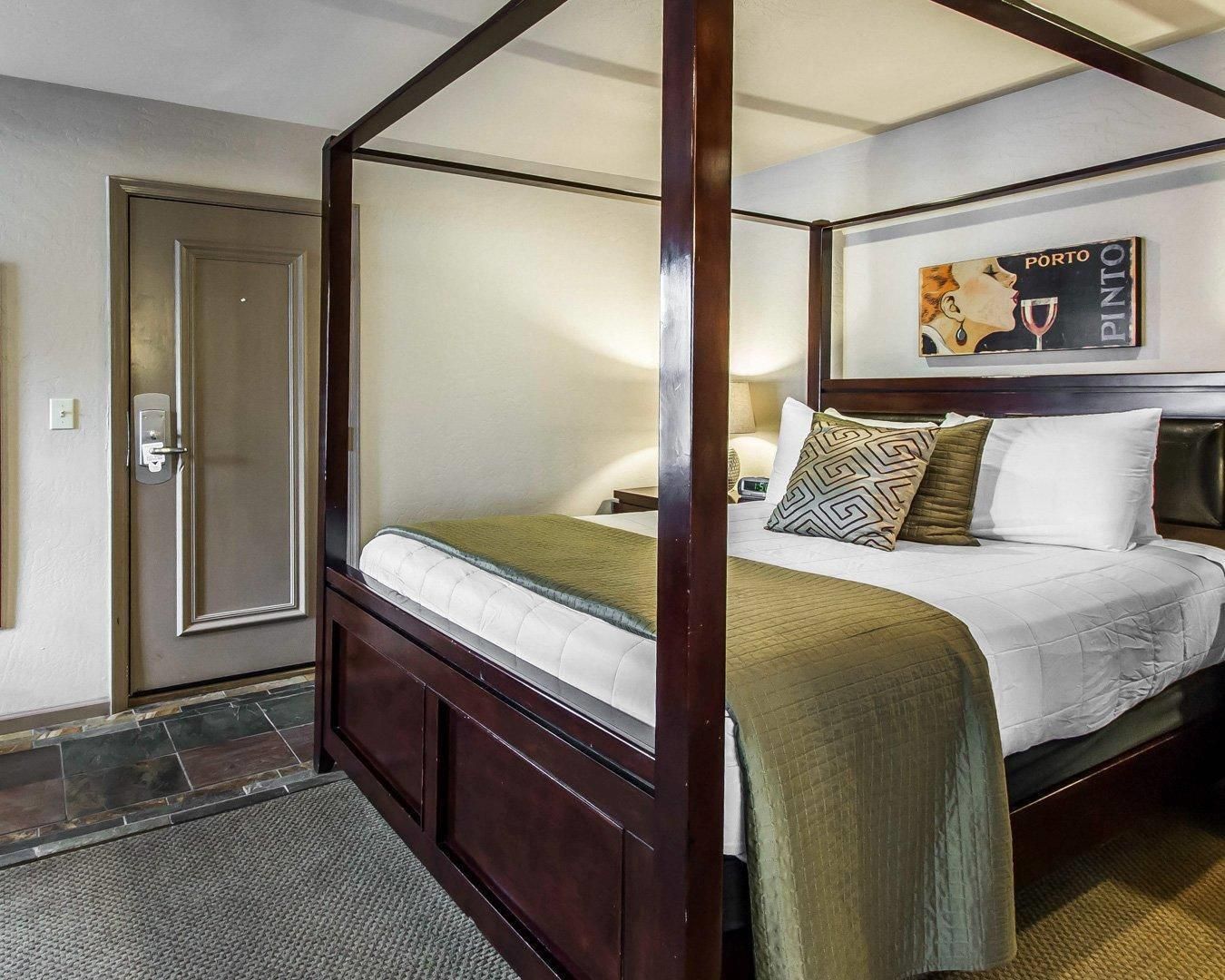 A four-poster bed with a headboard, a bedside table, and a wall-mounted artwork.