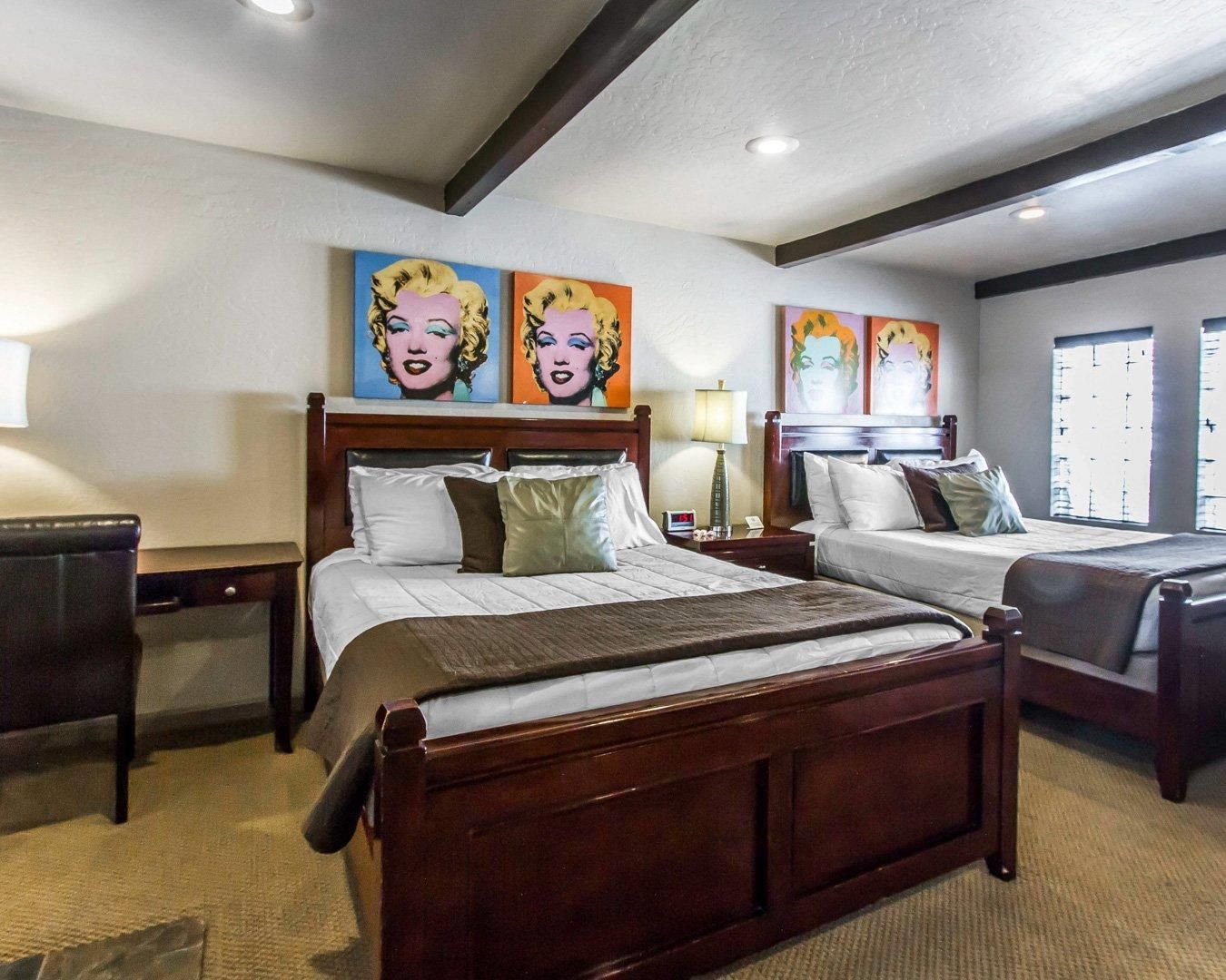 A hotel room with two beds, a wooden headboard, and artwork on the walls.