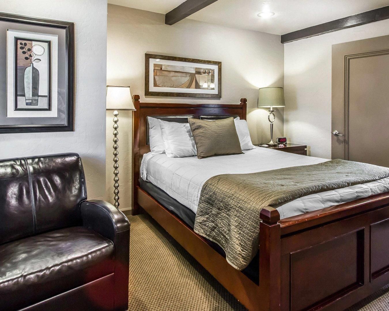 A hotel room with a bed, a nightstand, a lamp, a framed picture, and a door.