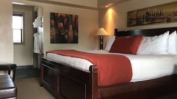 Habitación de hotel con una cama grande, una mesita de noche, una lámpara, un cuadro en la pared y una ventana con persianas.