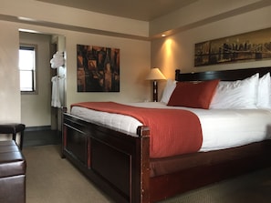 A hotel room with a large bed, a nightstand, a lamp, a painting on the wall, and a window with blinds. - Rodeway Inn & Suites Williams Downtowner - Rte 66 (Williams)