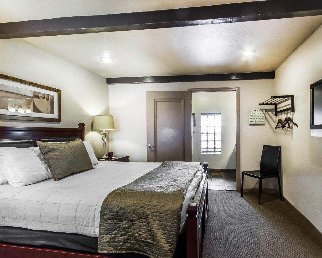 A hotel room with a bed, a nightstand, a lamp, a chair, a door, and a window.