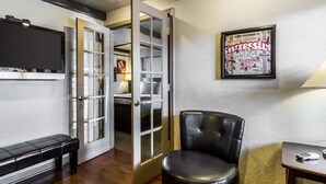 A room with a black leather chair, a bench, a TV mounted on the wall, and a framed poster. - Rodeway Inn & Suites Williams Downtowner - Rte 66 (Williams)