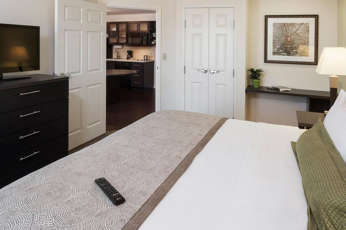 A hotel room with a bed, a TV, a desk, and a kitchenette.