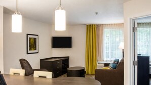 A hotel room with a dining table, chairs, a sofa, a TV, and a window with curtains. - Candlewood Suites Pearl by IHG (Pearl)