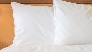 Uma cama com roupa de cama branca e cabeceira de madeira.
